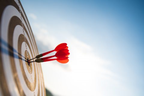 Close up shot red darts arrows in the target center on dark blue sky background. Business target or website design goal concept.