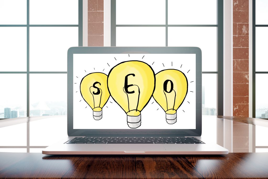 Laptop with drawn seo lamps on screen placed on wooden desktop. Window with city view in the background. Search engine optimization concept.