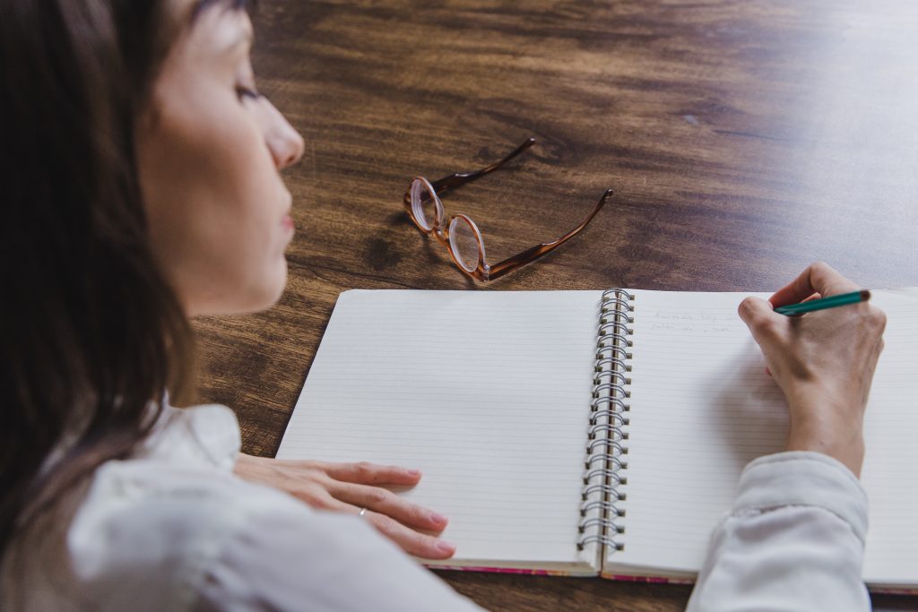 woman writing in coil notebook while brainstorming keyphrases